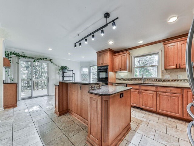 kitchen with backsplash, a center island, dark stone counters, and sink