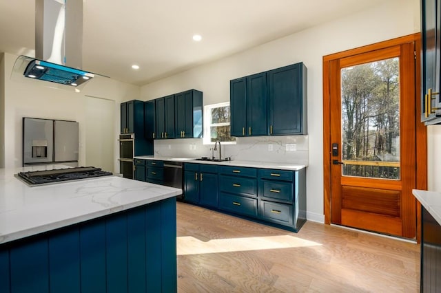 kitchen featuring appliances with stainless steel finishes, tasteful backsplash, sink, island exhaust hood, and blue cabinetry