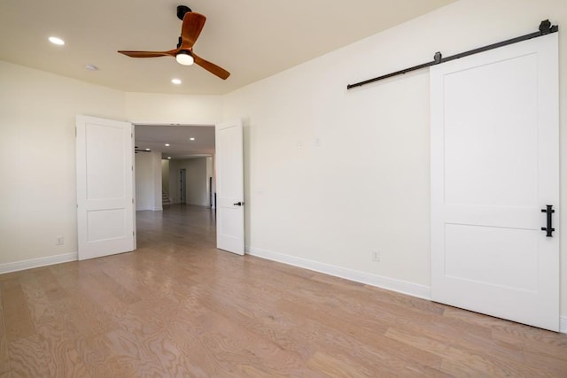 unfurnished bedroom with light hardwood / wood-style floors, a barn door, and ceiling fan