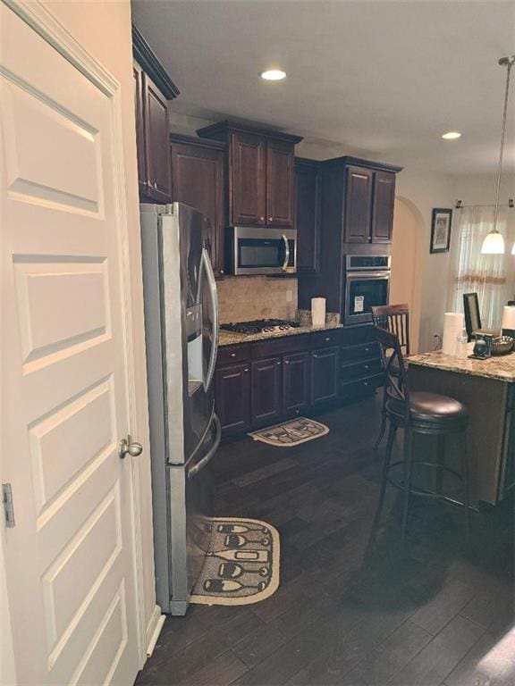 kitchen with pendant lighting, dark hardwood / wood-style floors, light stone countertops, appliances with stainless steel finishes, and dark brown cabinets