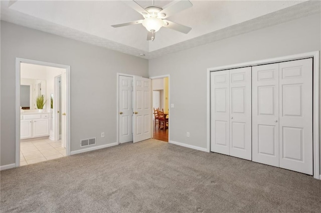 unfurnished bedroom with ceiling fan, light carpet, ensuite bath, and a tray ceiling