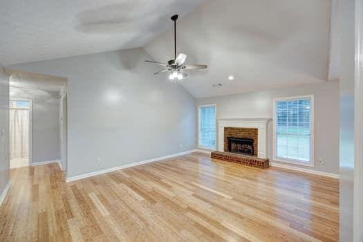 2105 Huntington Hills Trce, Buford, GA 30519 - unfurnished living room featuring a ceiling fan, light wood-style flooring, a brick fireplace, and high vaulted ceiling