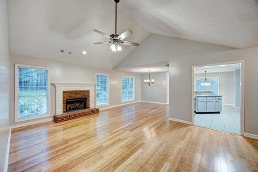 2105 Huntington Hills Trce, Buford, GA 30519 - unfurnished living room featuring a chandelier, ceiling fan, light wood-type flooring, a brick fireplace, and high vaulted ceiling