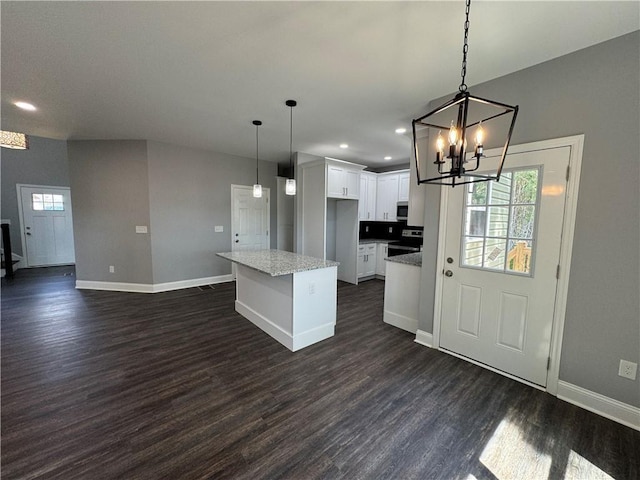 kitchen with hanging light fixtures, white cabinetry, a kitchen island, light stone countertops, and dark hardwood / wood-style floors