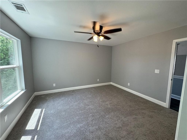 empty room with dark carpet, ceiling fan, and a wealth of natural light