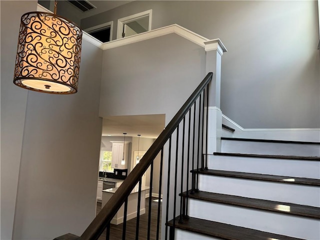 staircase featuring wood-type flooring, a high ceiling, and sink