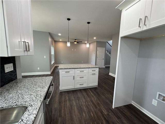 kitchen featuring light stone counters, white cabinets, pendant lighting, dark wood-type flooring, and a fireplace