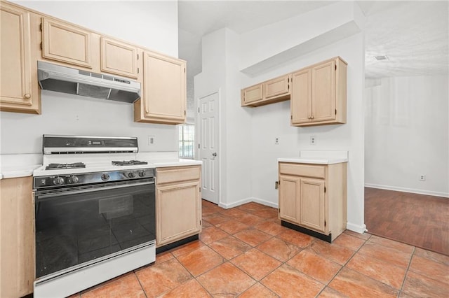 kitchen featuring under cabinet range hood, light brown cabinets, light countertops, and gas stove