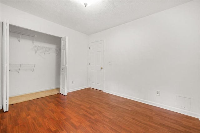 unfurnished bedroom featuring a textured ceiling, wood finished floors, baseboards, and a closet