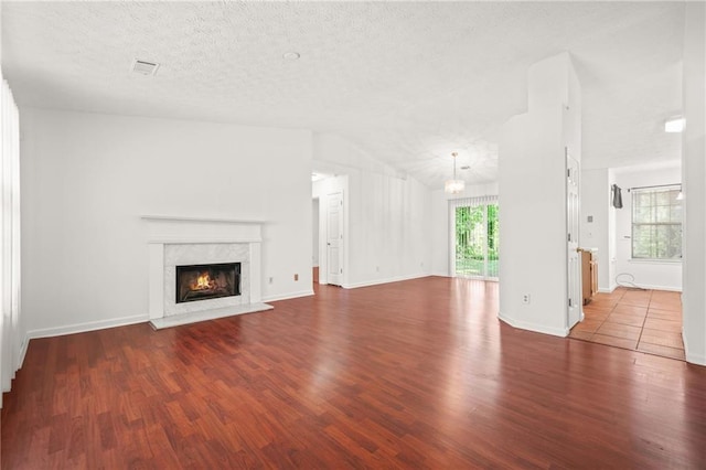 unfurnished living room featuring an inviting chandelier, a fireplace, a textured ceiling, visible vents, and wood finished floors
