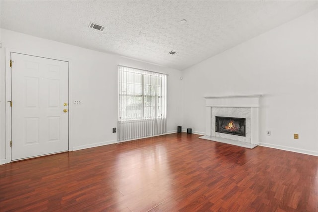 unfurnished living room with a premium fireplace, a textured ceiling, wood finished floors, and visible vents