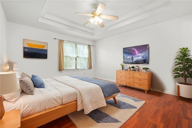 bedroom with a raised ceiling, wood finished floors, baseboards, and a ceiling fan