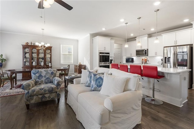 living room with dark wood finished floors, recessed lighting, ceiling fan with notable chandelier, and crown molding