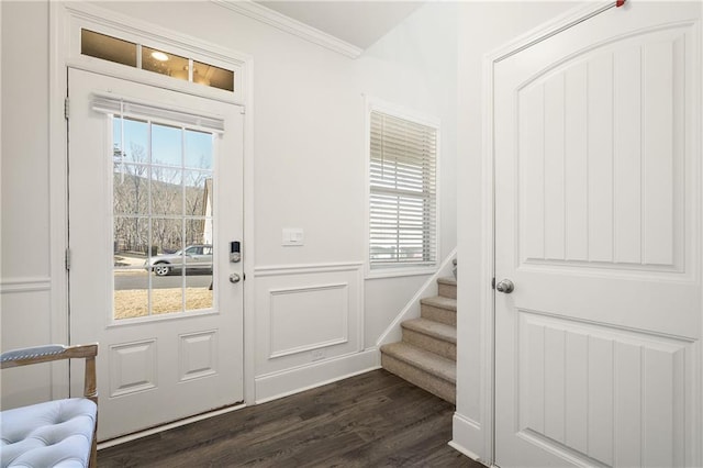 foyer entrance with plenty of natural light, dark wood-type flooring, ornamental molding, and stairs