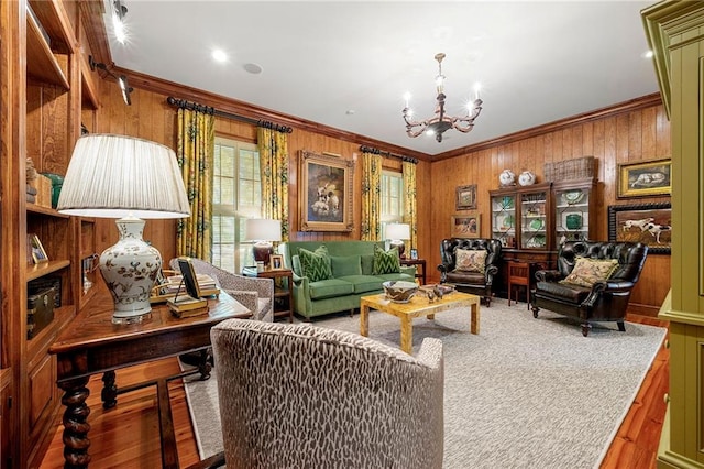 living area featuring wood-type flooring, ornamental molding, an inviting chandelier, and wooden walls