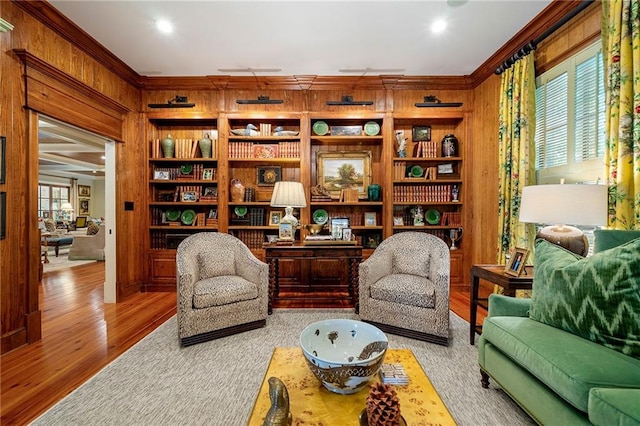 sitting room featuring ornamental molding, hardwood / wood-style flooring, built in shelves, and wooden walls