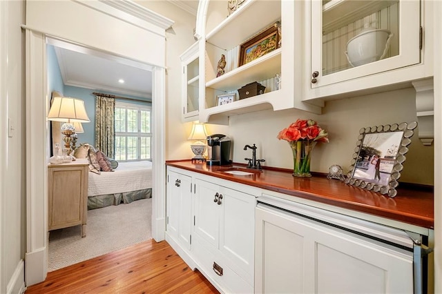 bar featuring white cabinets, light wood-type flooring, crown molding, wood counters, and sink