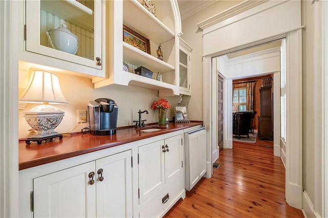 bar with light hardwood / wood-style flooring, sink, crown molding, and white cabinetry