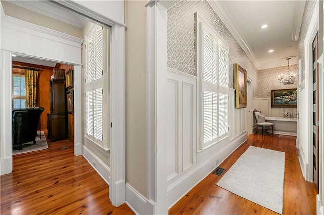 corridor with hardwood / wood-style floors, a notable chandelier, and crown molding