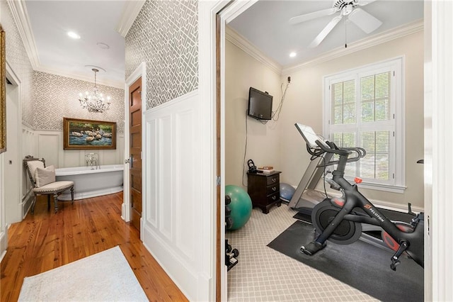 exercise area featuring ceiling fan with notable chandelier, hardwood / wood-style flooring, and ornamental molding