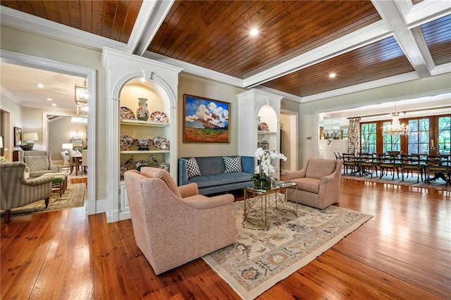 living room featuring beamed ceiling, crown molding, built in features, hardwood / wood-style flooring, and an inviting chandelier