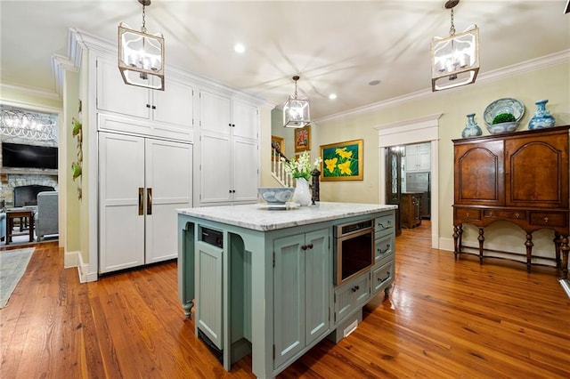 kitchen with a brick fireplace, a kitchen island, green cabinetry, hardwood / wood-style flooring, and white cabinetry