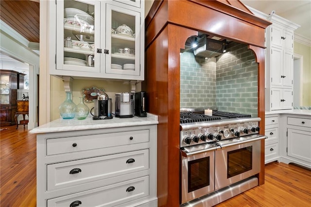 kitchen featuring double oven range, tasteful backsplash, white cabinets, light wood-type flooring, and ornamental molding