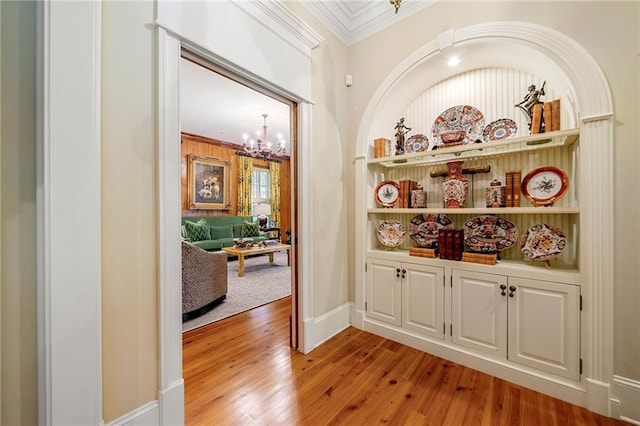 corridor featuring an inviting chandelier, light hardwood / wood-style floors, and crown molding