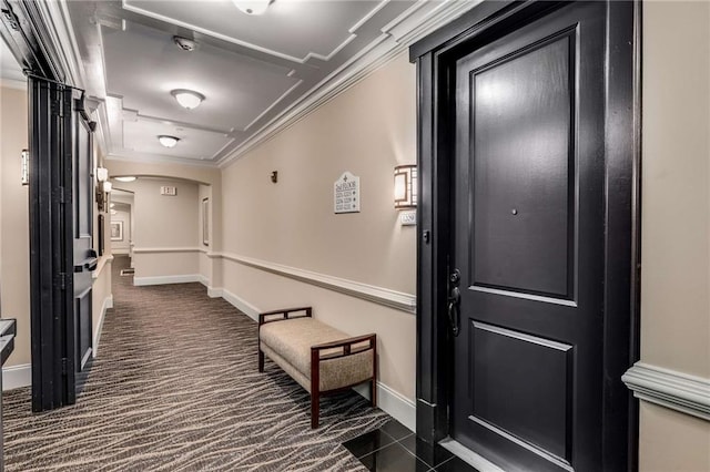 hallway with arched walkways, baseboards, crown molding, and dark colored carpet