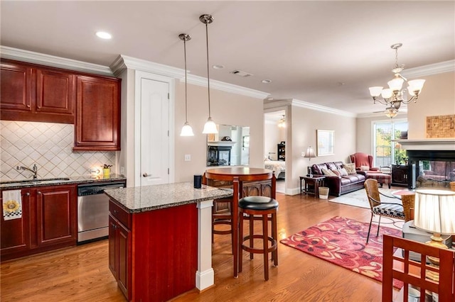 kitchen with hanging light fixtures, stainless steel dishwasher, sink, and a multi sided fireplace