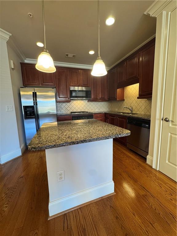 kitchen with dark wood-style floors, appliances with stainless steel finishes, a kitchen island, and crown molding