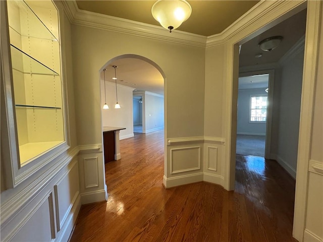 corridor with arched walkways, a wainscoted wall, ornamental molding, dark wood-type flooring, and a decorative wall