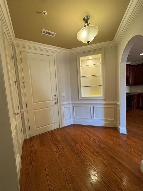 interior space featuring arched walkways, a decorative wall, wood finished floors, visible vents, and ornamental molding
