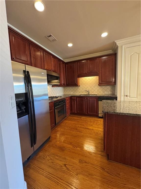 kitchen featuring visible vents, appliances with stainless steel finishes, dark stone countertops, wood finished floors, and a sink