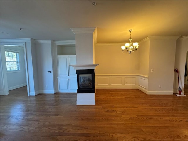 unfurnished living room featuring a chandelier, ornamental molding, dark wood finished floors, and a glass covered fireplace