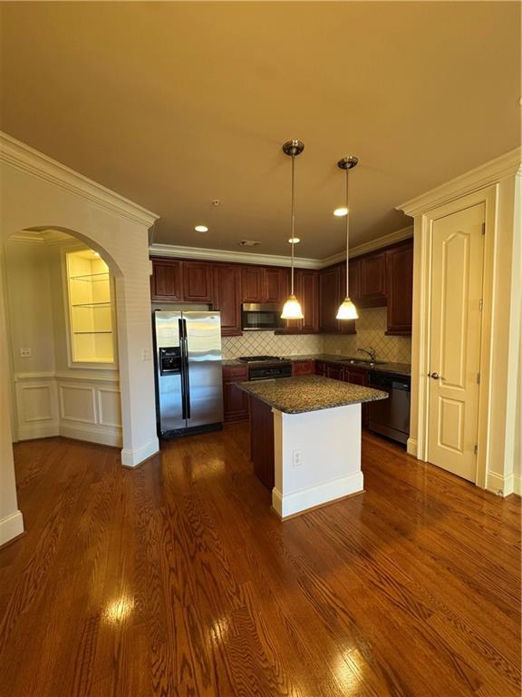 kitchen featuring arched walkways, crown molding, dark wood finished floors, stainless steel appliances, and a sink