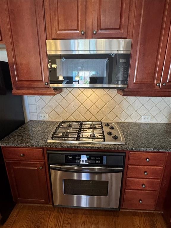 kitchen featuring dark wood-style floors, tasteful backsplash, appliances with stainless steel finishes, and dark stone countertops