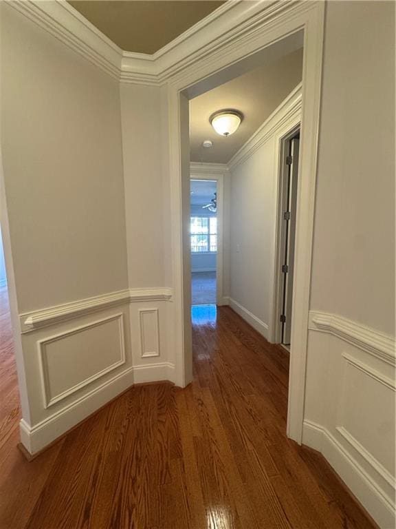 corridor with a wainscoted wall, a decorative wall, crown molding, and wood finished floors