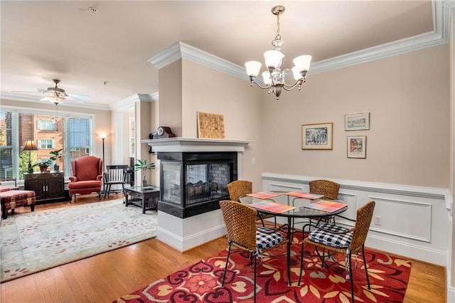 dining room featuring crown molding, light hardwood / wood-style flooring, ceiling fan with notable chandelier, and a multi sided fireplace