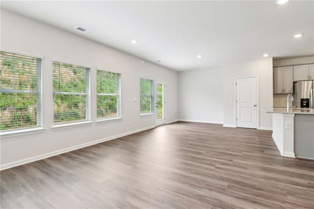 unfurnished living room with a sink, wood finished floors, visible vents, recessed lighting, and baseboards