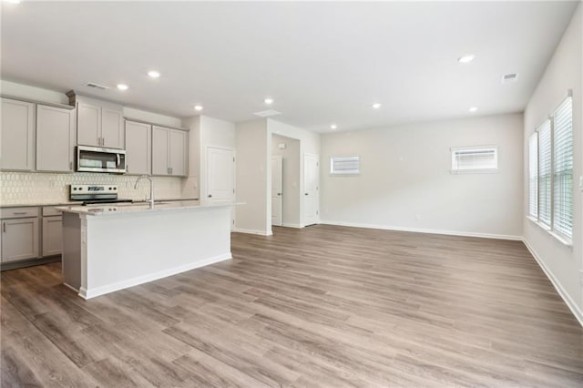 kitchen featuring appliances with stainless steel finishes, a sink, backsplash, an island with sink, and gray cabinets