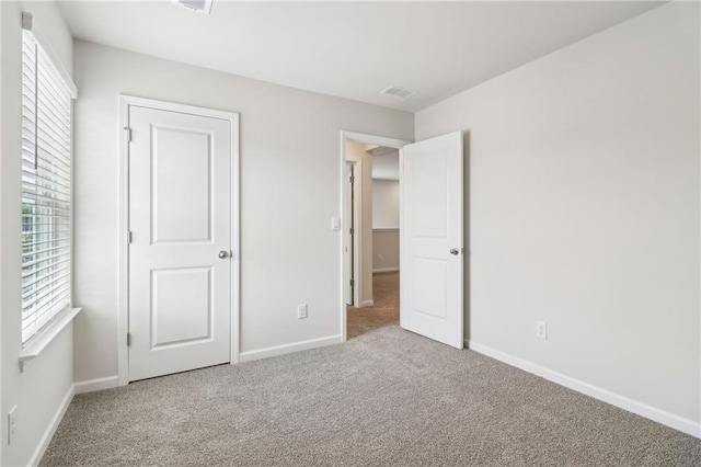 unfurnished bedroom featuring carpet flooring, multiple windows, and visible vents