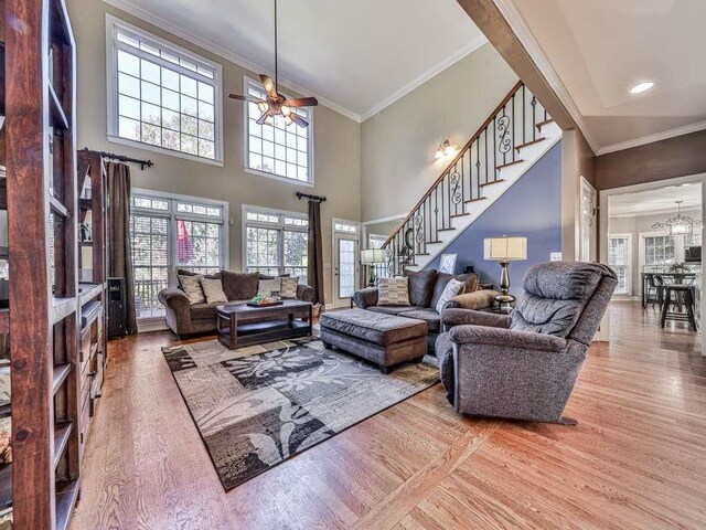 living room featuring hardwood / wood-style floors, ceiling fan with notable chandelier, ornamental molding, and a towering ceiling