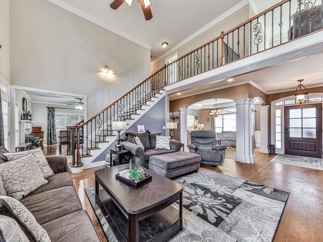 living room featuring wood-type flooring, a towering ceiling, decorative columns, and ornamental molding