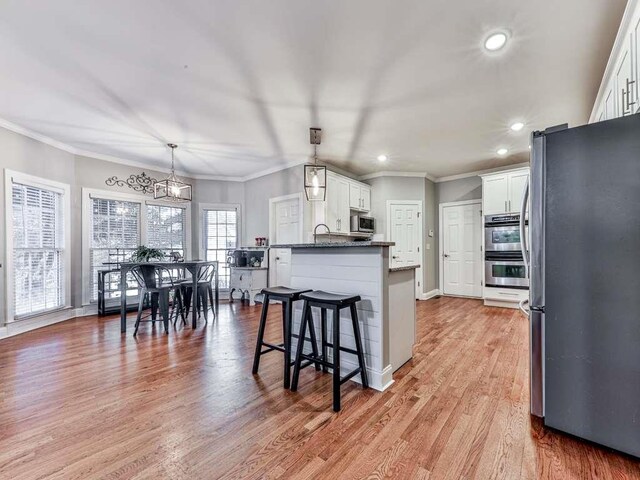 kitchen featuring white cabinets, appliances with stainless steel finishes, light wood-type flooring, and decorative light fixtures