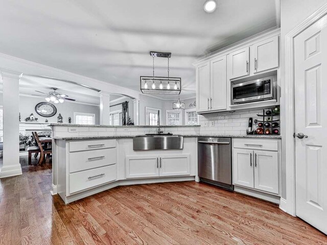 kitchen with ornate columns, white cabinetry, sink, stainless steel appliances, and light wood-type flooring