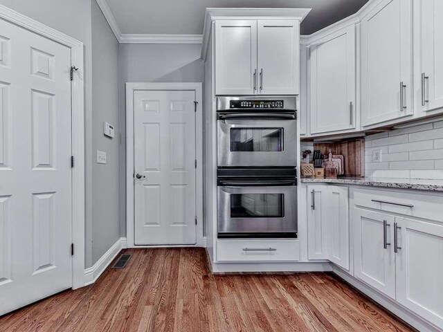 kitchen featuring white cabinets, stainless steel double oven, light hardwood / wood-style floors, and light stone counters