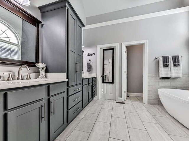 bathroom with a bathing tub, vanity, tile walls, and tile patterned flooring