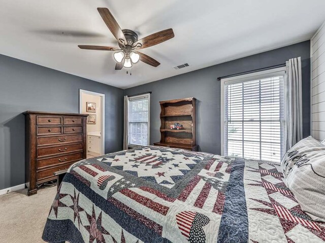 carpeted bedroom with multiple windows, ensuite bath, and ceiling fan