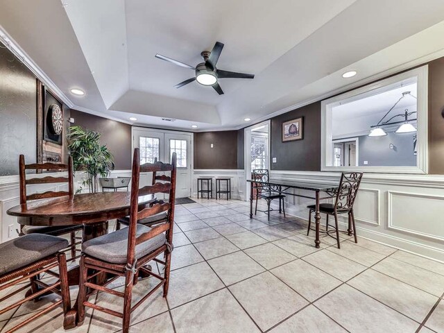 tiled dining space with french doors, a tray ceiling, ceiling fan, and ornamental molding